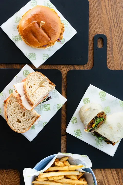 Overhead view of burger, sandwich, wrap, and fries on black trays.