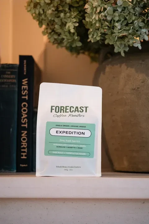 White 'FORECAST Coffee' bag from Peru, with books and a vase.