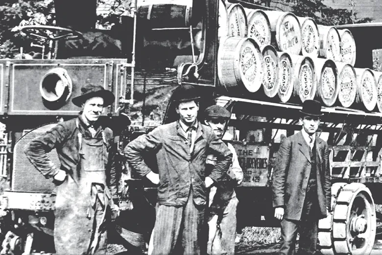 Historical photo: Four men with early truck carrying beverage barrels.