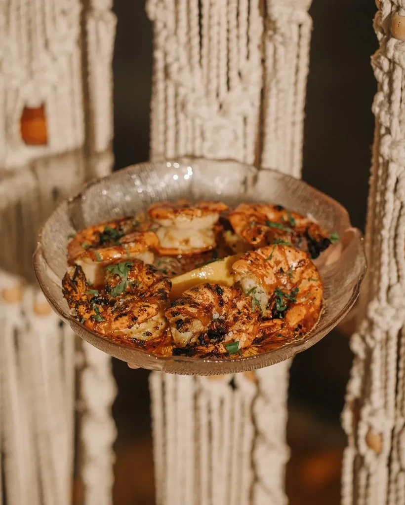 Grilled shrimp in a textured glass bowl with herbs and lemon.