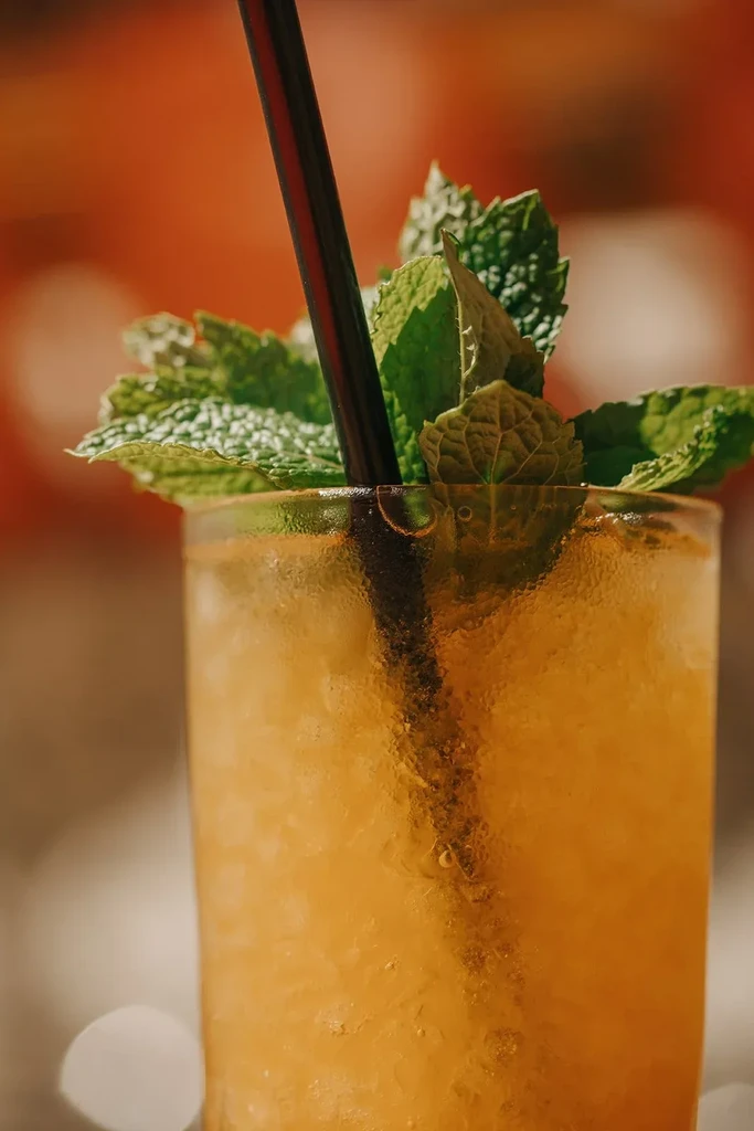 Tall frosty glass of amber liquid with mint and a straw.