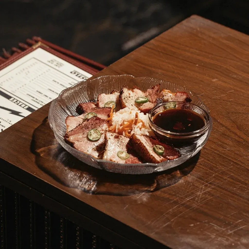 Sliced cooked meat, chili, slaw, and dipping sauce in glass bowl.