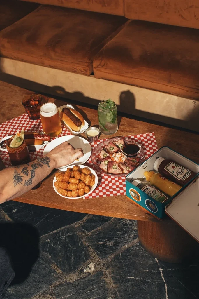 Table spread with hot dogs, tater tots, roasted meat, and cocktails.