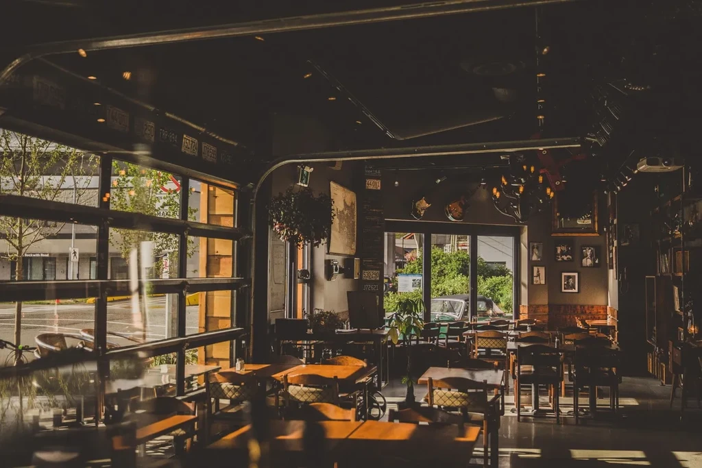Sunlit empty restaurant with rustic-industrial decor and open street-facing windows.