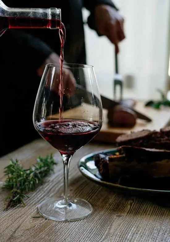 Red wine pours into glass; person carves meat, holds bottle.