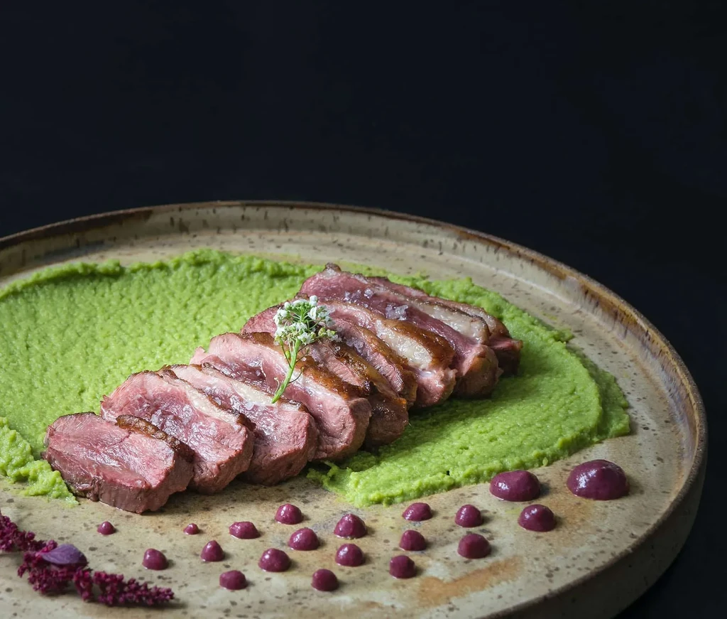 Fanned medium-rare meat, green puree, purple sauce, floral garnish.
