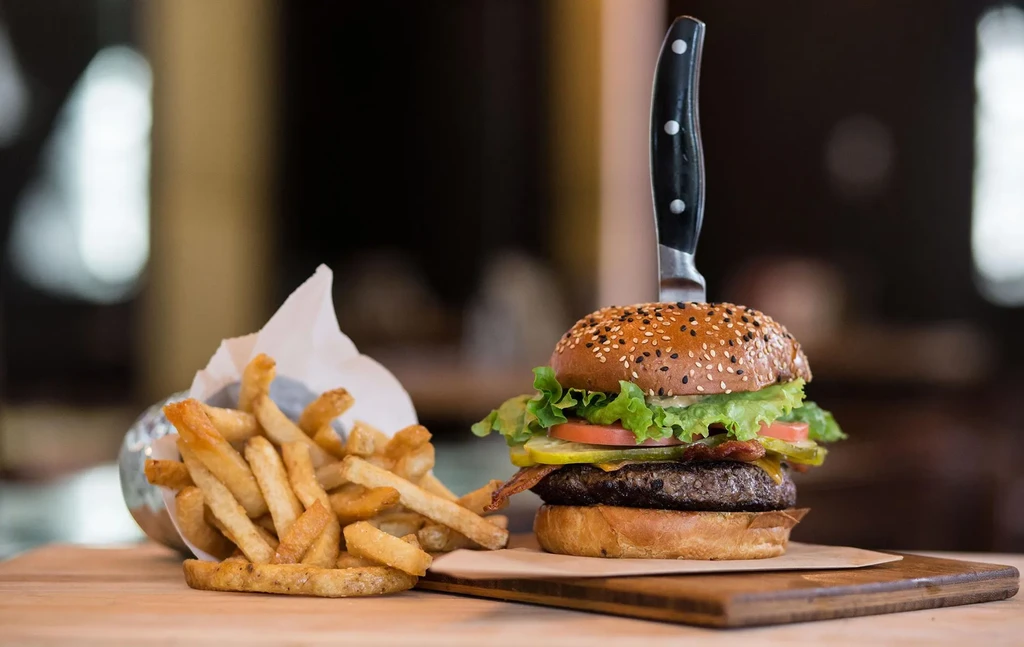 Close-up of gourmet burger with knife, fries on wooden board.
