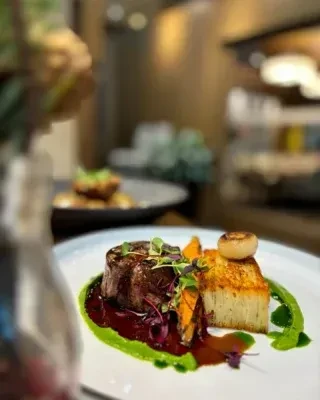 Artfully plated steak, potato gratin, vegetables, two sauces, in restaurant.