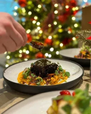 Hand drizzles sauce on plated dark meat, orange puree, and garnishes.