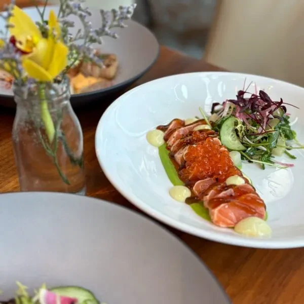 Plated seared salmon with ikura, green puree, yellow sauce, and salad.