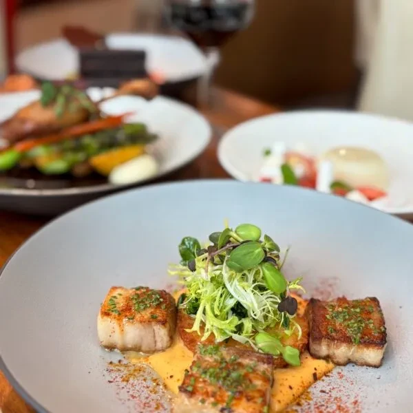 Gourmet seared scallops and pork belly dish in a fine dining setting.