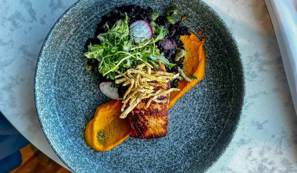 Seared fish with crispy topping, orange puree, dark rice, and salad.