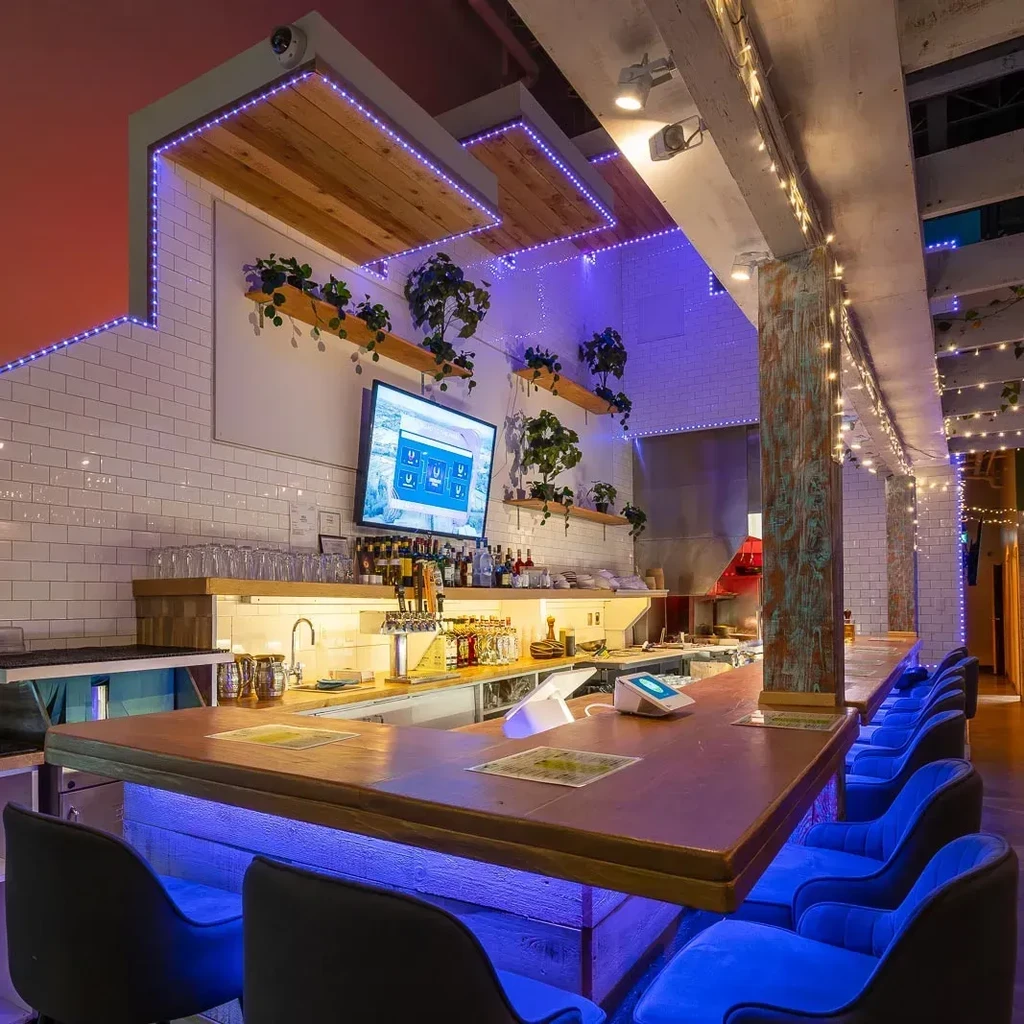 Modern bar with blue-lit counter, purple ceiling, and digital menu.