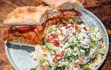 Ciabatta sandwich with fried protein and feta-topped side salad.