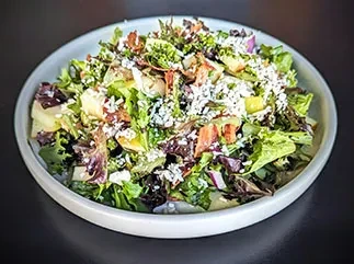 Colorful salad with greens, white cheese, diced fruit, and bacon bits.