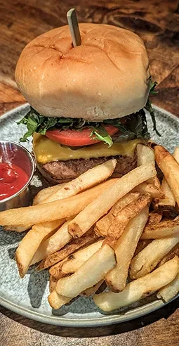 Burger with melted cheese, fries, and ketchup on a wooden table.