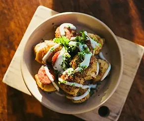 Potato pieces with sausage, white sauce, and herbs in a rustic bowl.