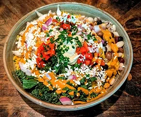 Vibrant salad bowl with beans, greens, cheese, hummus, and drizzled sauce.