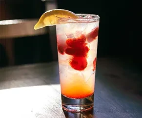 Tall glass of sparkling drink with red berries, ice, and lemon.