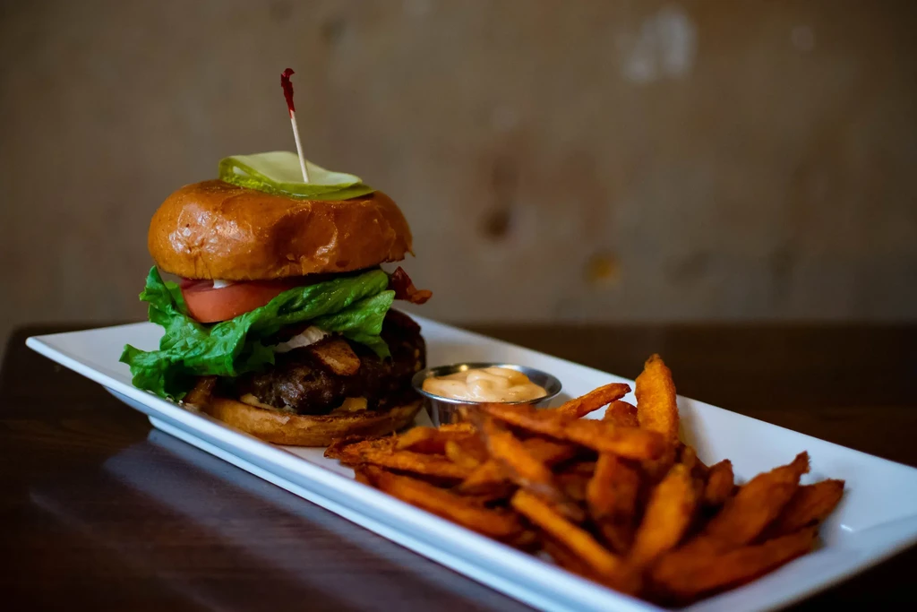 Gourmet burger, sweet potato fries, and dipping sauce on a white plate.