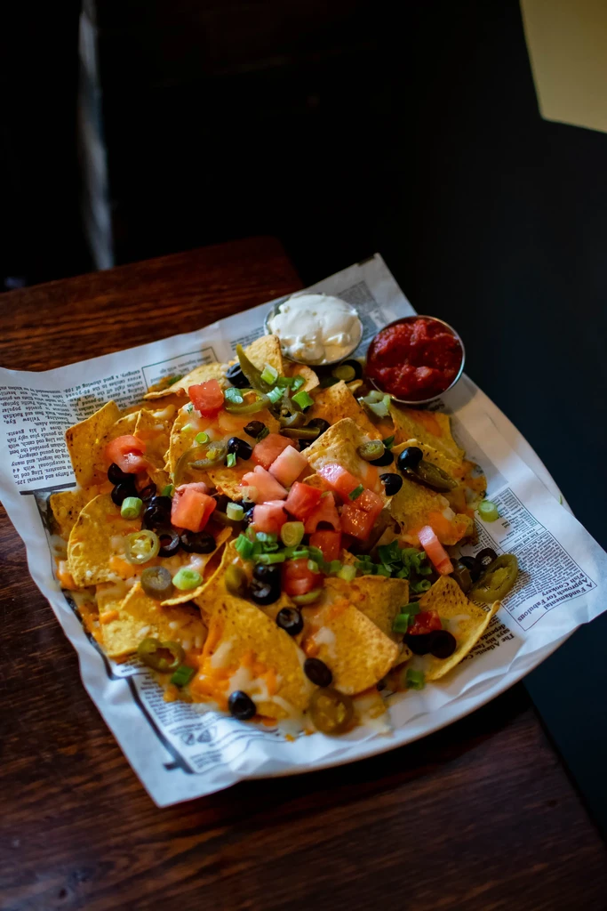 Nachos on newspaper-lined plate with cheese, veggies, sour cream, and salsa.