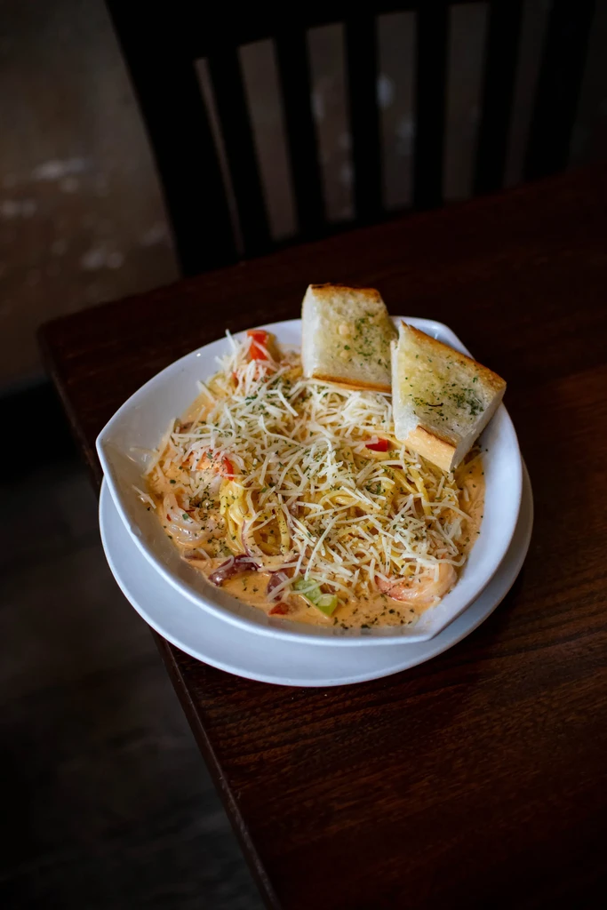 Creamy pasta with cheese, peppers, and garlic bread on a dark table.