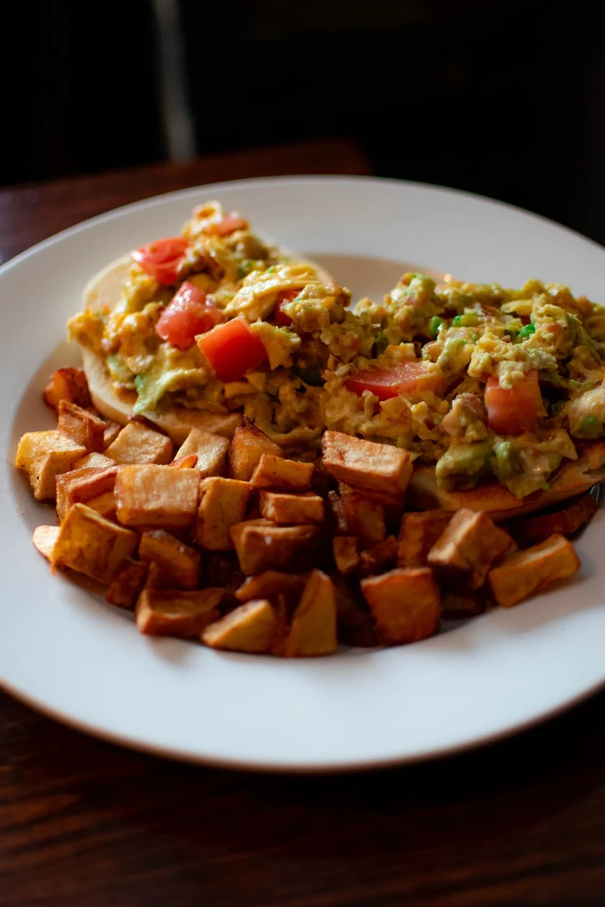 Breakfast plate with scrambled eggs, avocado, tomatoes, and home fries.
