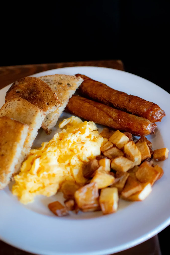 A plate of scrambled eggs, browned sausages, home fries, and toast.