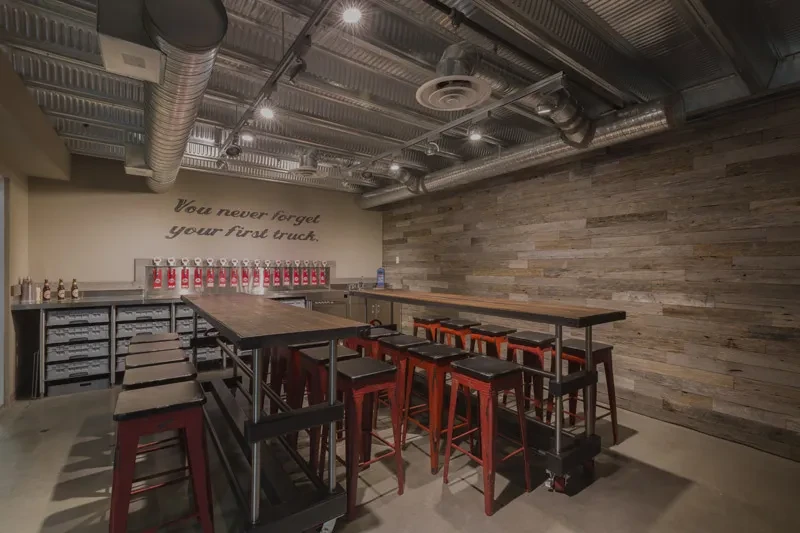 Industrial-rustic taproom interior with high tables, red stools, beer taps.