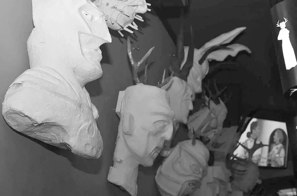 Black and white: white antlered plaster busts on dark wall.