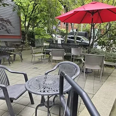 Empty outdoor cafe patio with ornate dark grey furniture and red umbrella.