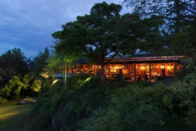 Lush hillside restaurant glowing warmly at dusk.