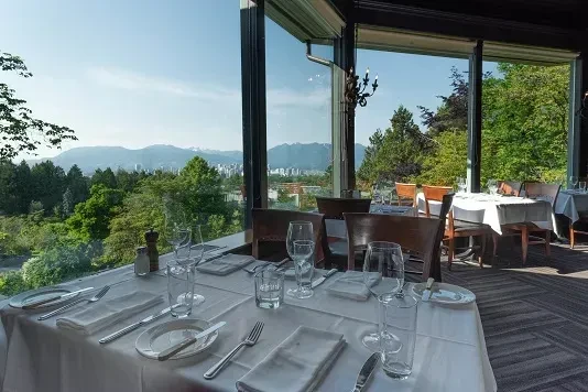Elegant restaurant interior with panoramic view of city, mountains, and trees.