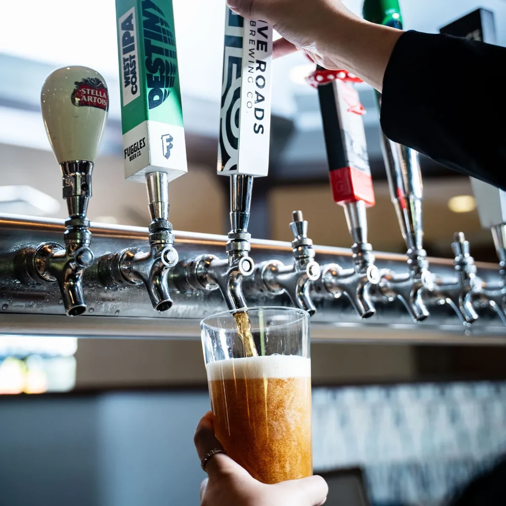 Hand pours frothy golden beer from a bar tap system.