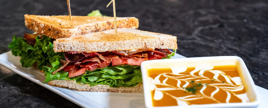 Half BLT-style sandwich and orange soup with a cream swirl.