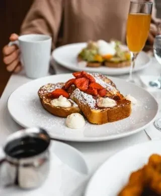 Golden French toast with strawberries, cream, coffee, mimosa on a white table.