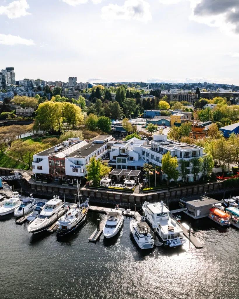 Sunny aerial view: Dockside waterfront complex, marina with boats, city.