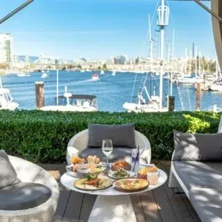 Outdoor table with food and chairs overlooks a harbor and city.
