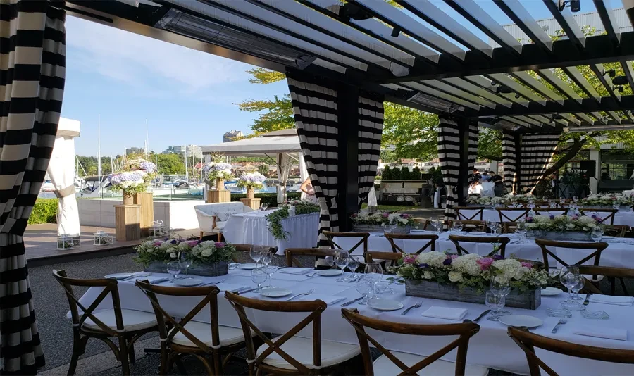 Outdoor tables with floral centerpieces under striped pergola at marina.