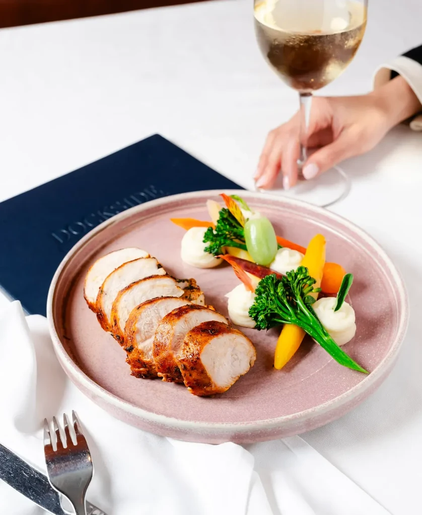 Plated chicken breast, vegetables, mashed potatoes, wine, and DOCKSIDE menu.