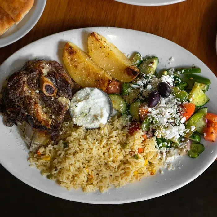Greek lamb shank meal with rice, tzatziki, salad, and feta.
