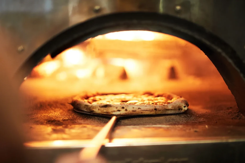 Cooked pizza on a peel in a hot, glowing oven.