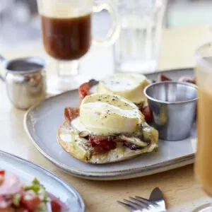 Close-up of Eggs Benedict, coffee, and juice on a wooden table.