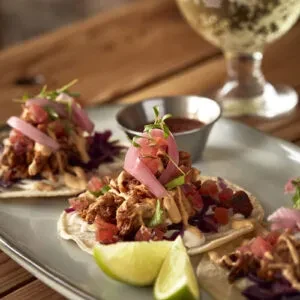 Three meat tacos with purple cabbage, pickled onions, and lime wedges.