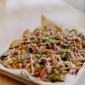Close-up of nachos with pulled meat, olives, tomatoes, and pickled onions.