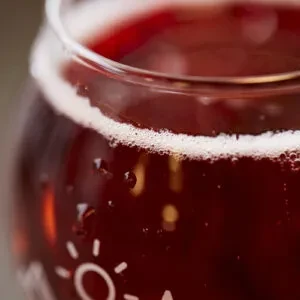 Close-up of a dark carbonated drink with a frothy head and condensation.