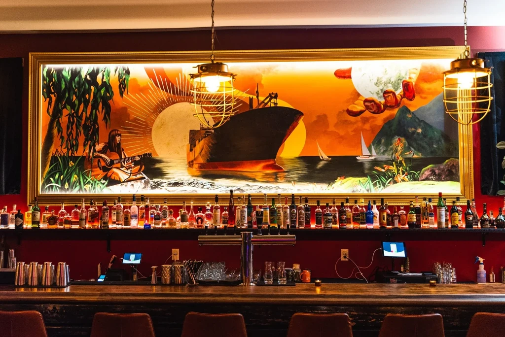 An artistic bar with a large, vibrant mural and illuminated liquor bottles.