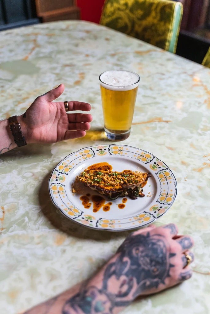 Hands reaching for a savory meal and beer on a marble table.
