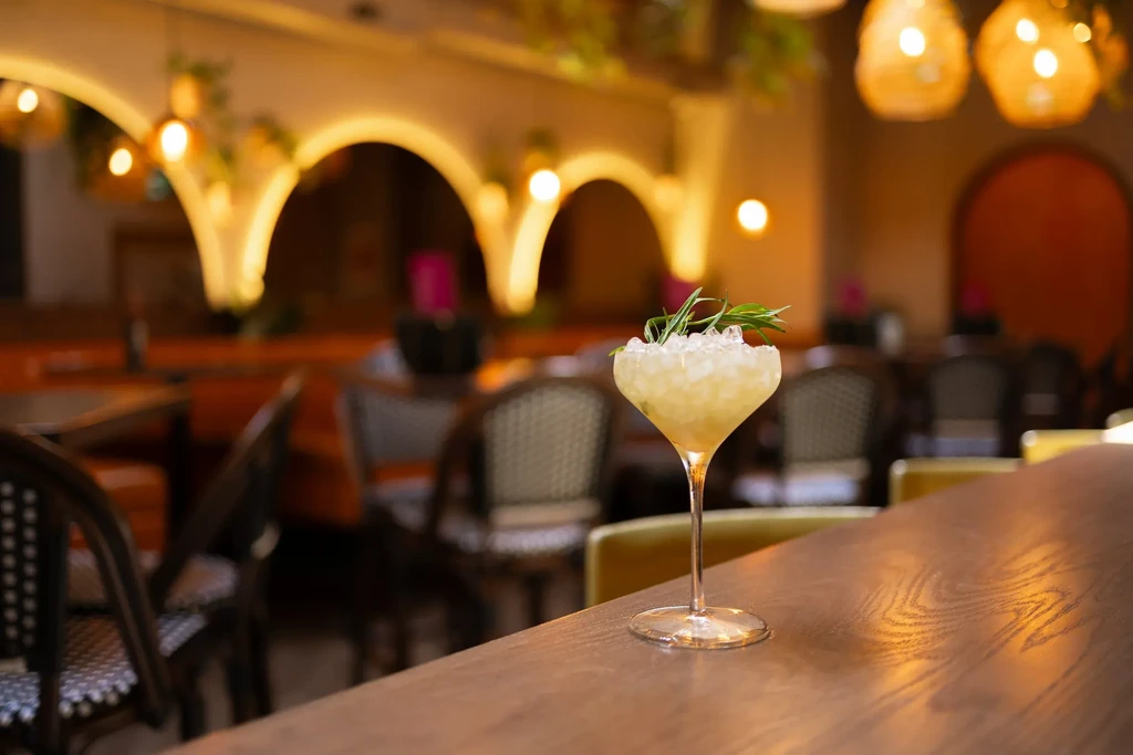 Rosemary cocktail on a bar, warm blurred restaurant background.
