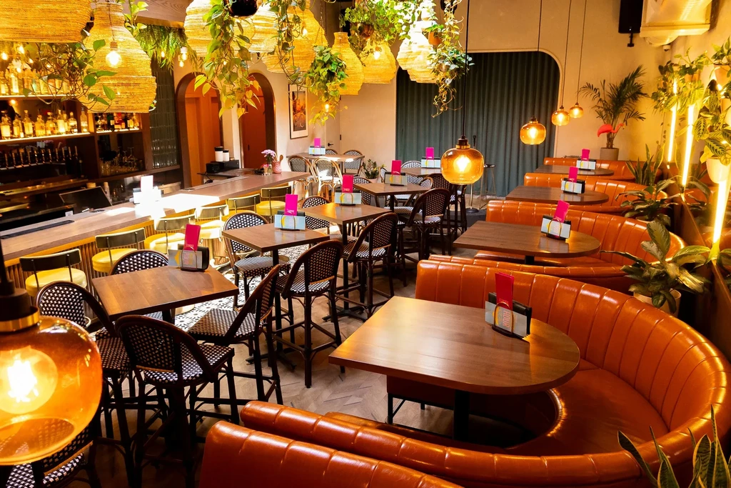 Empty modern restaurant interior with bar, varied seating, and lush plants.